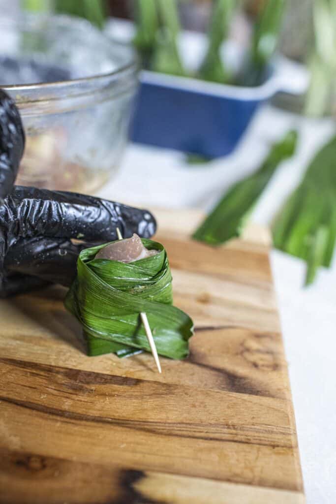 Hand holding tooth picked pandan leaves wrapped chicken.