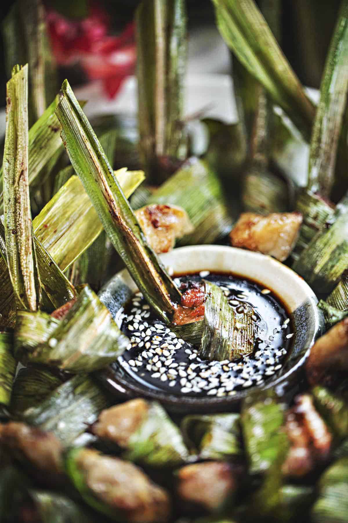 Wrapped pandan chicken on a plate with dark dipping sauce. 