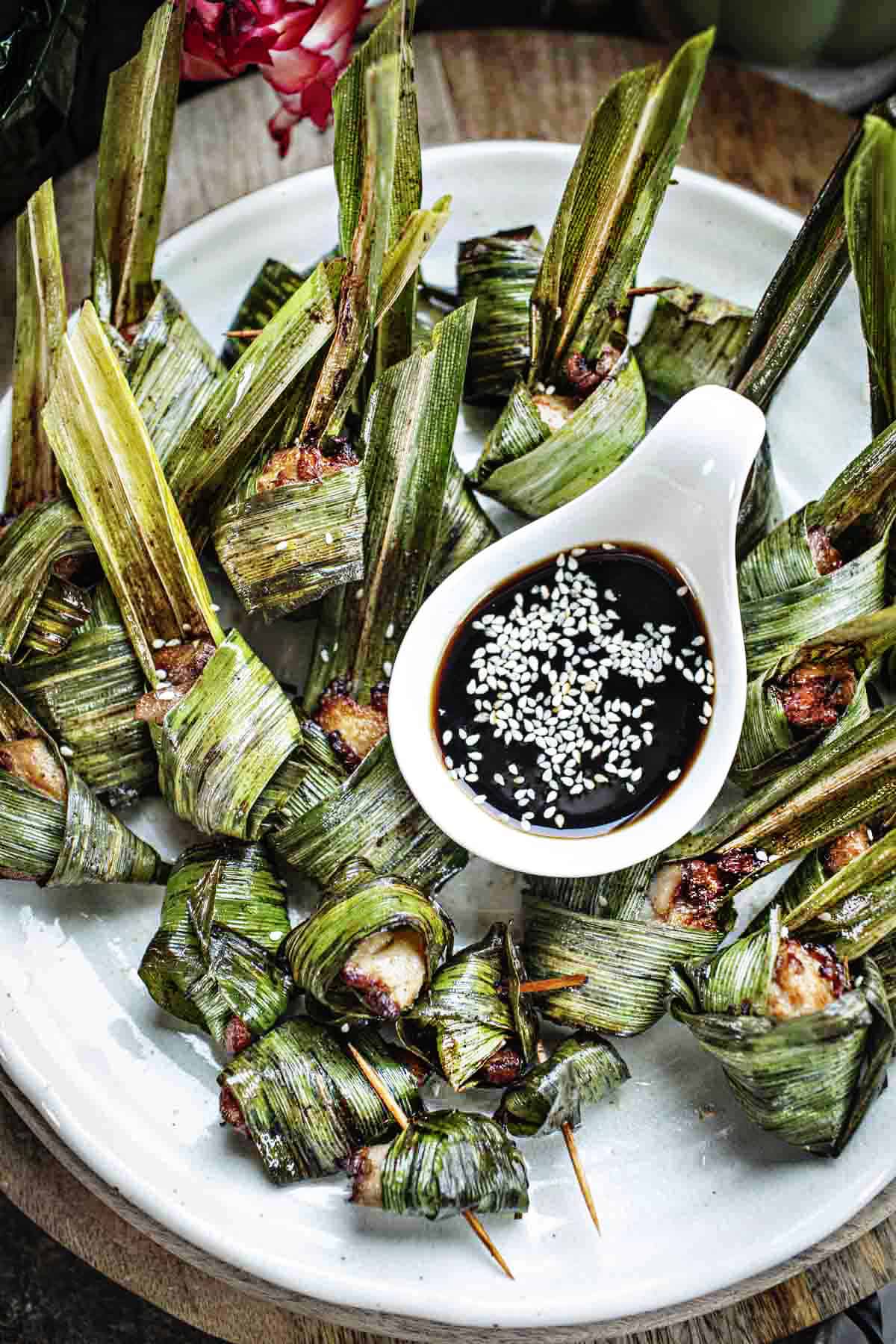 Wrapped pandan chicken on a plate with dark dipping sauce. 