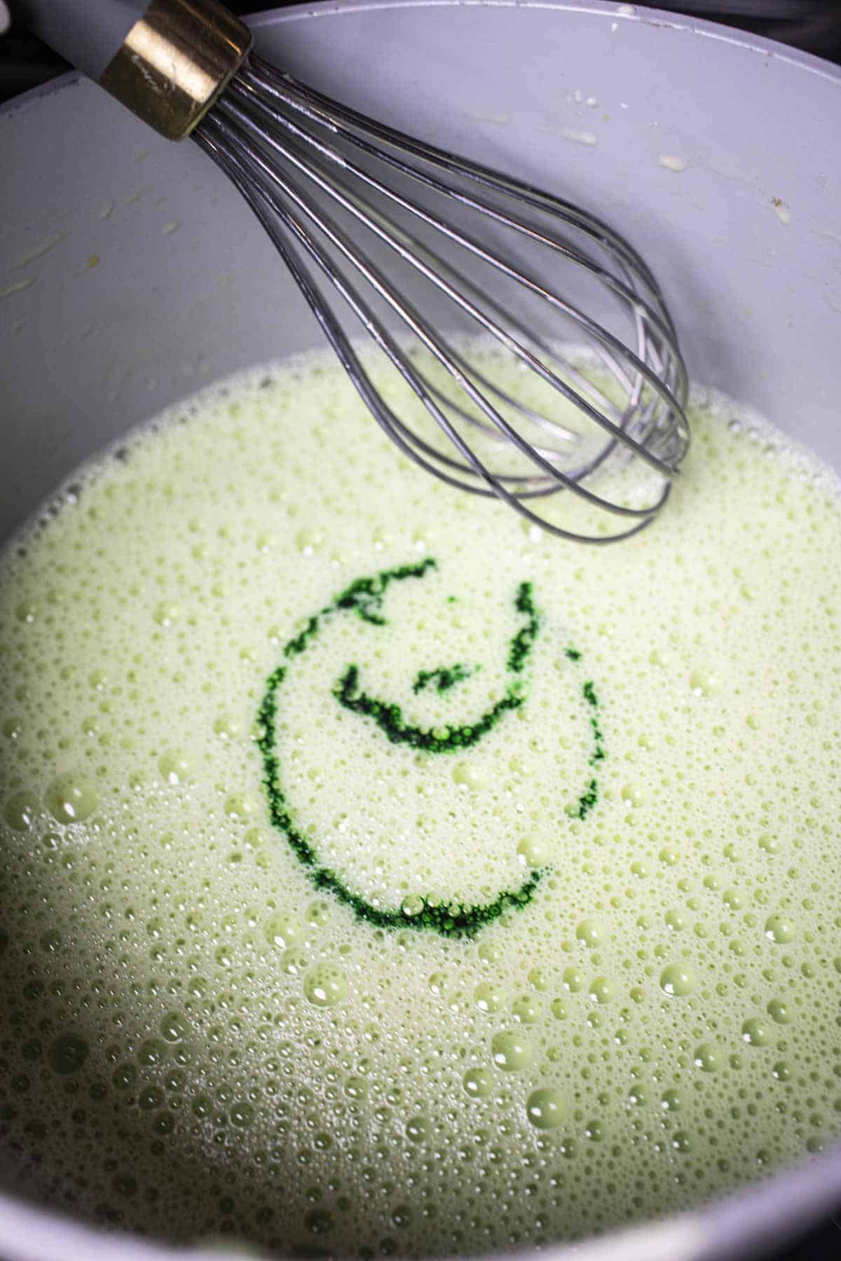 Egg and milk mixture in a pot with a whis and green color droplets. 