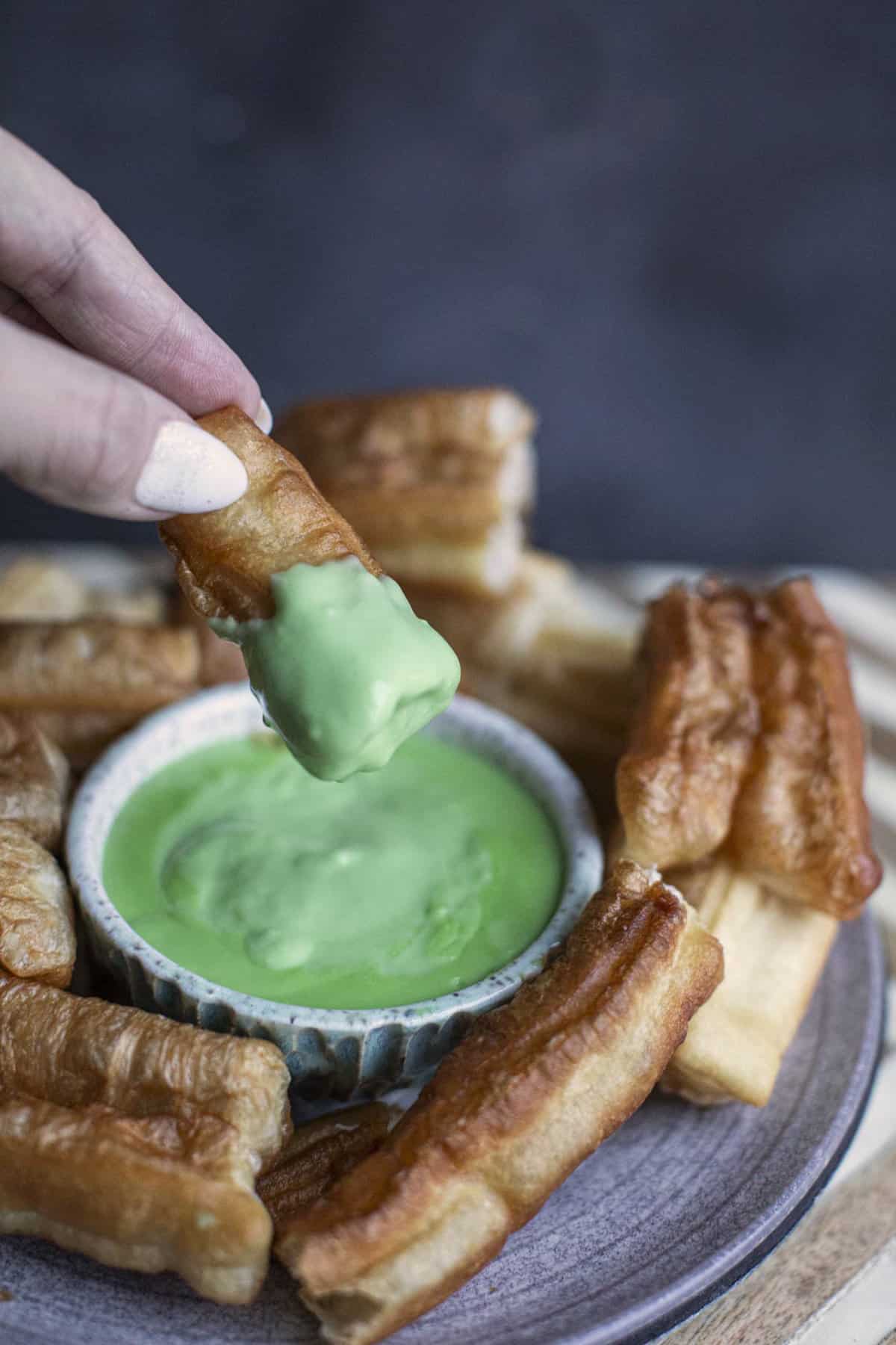 fingers lifting donut dipped in green pandan custard. 