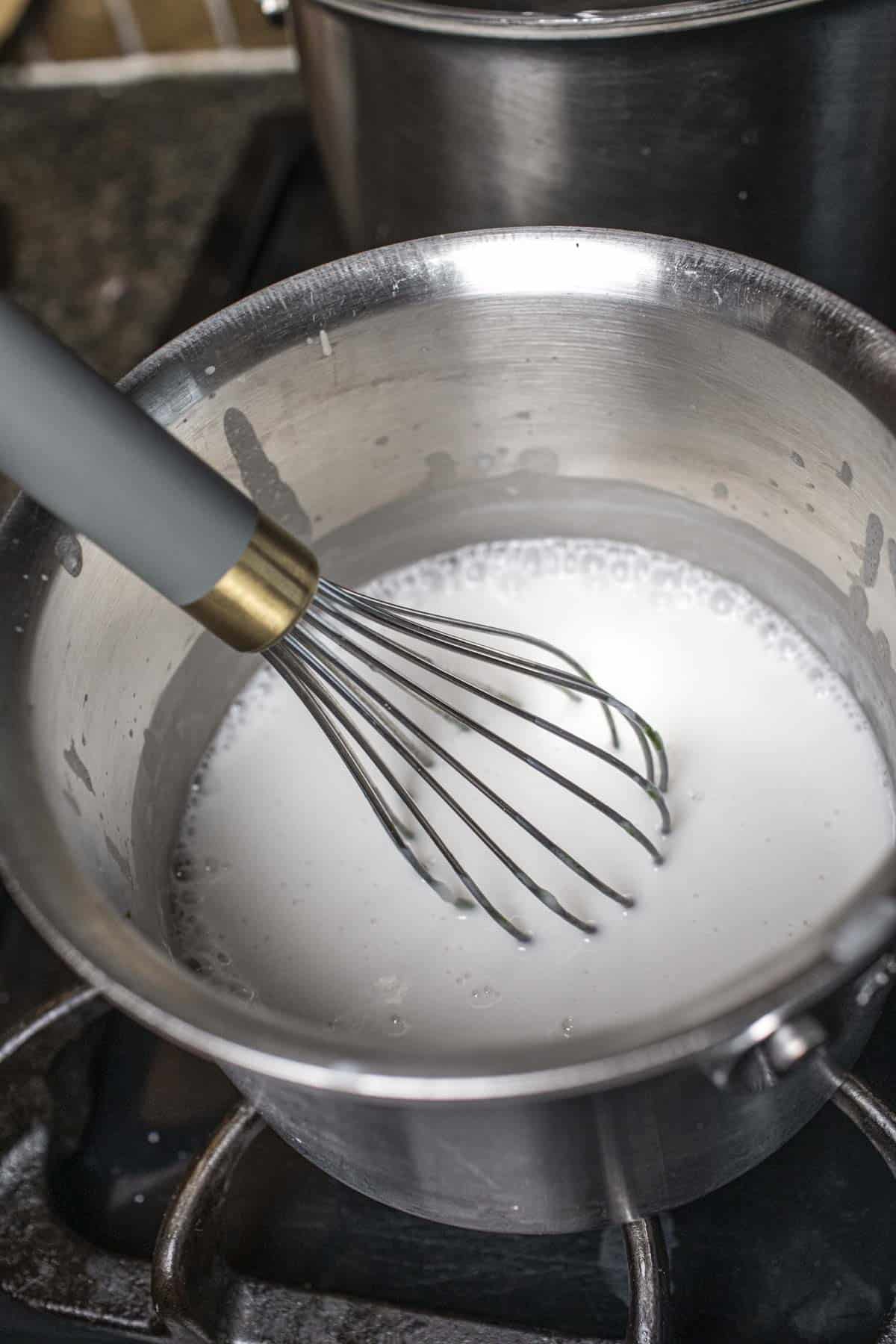 A whisk in a sauce pan with coconut milk.