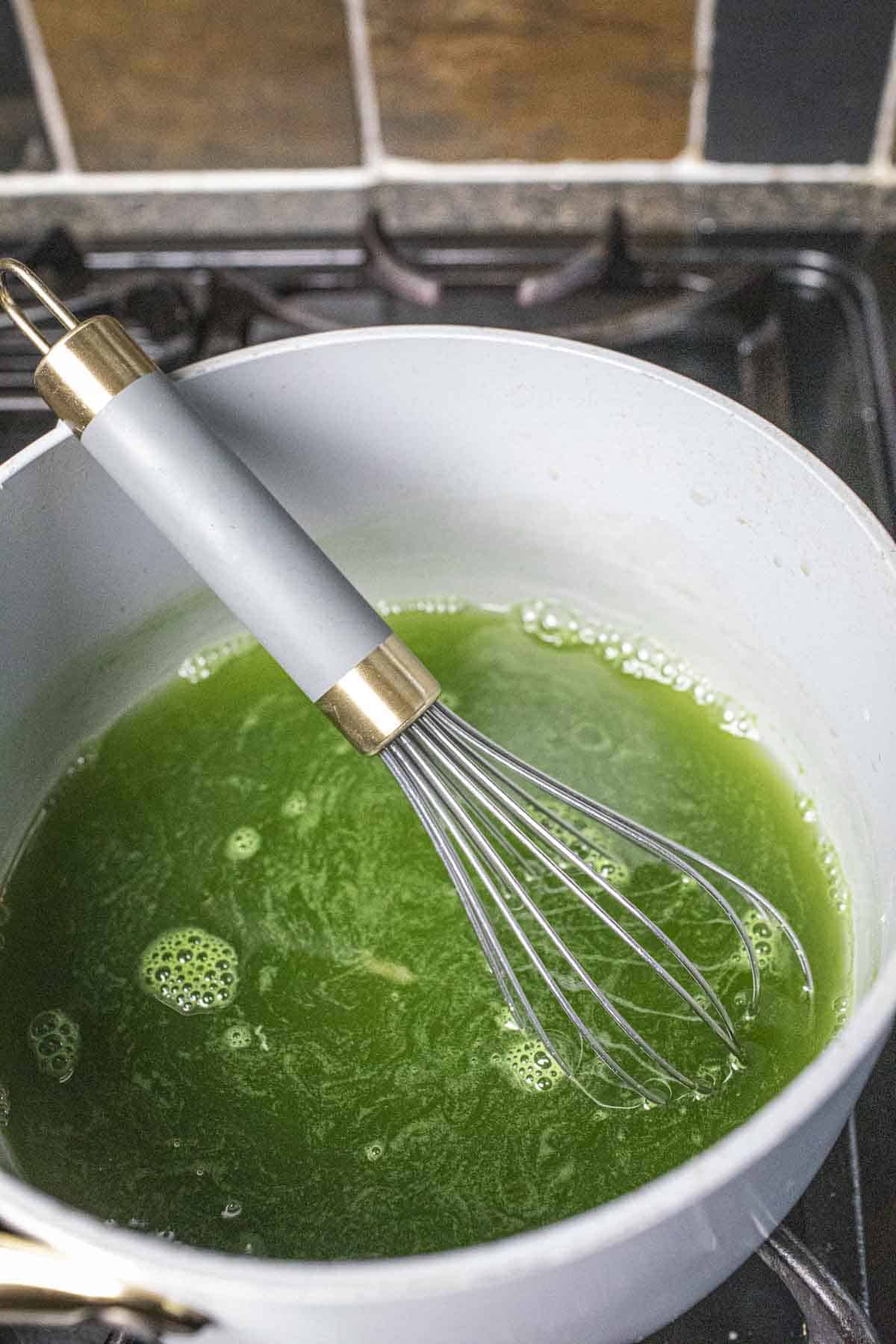 A whisk inside a pot with green pandan water. 