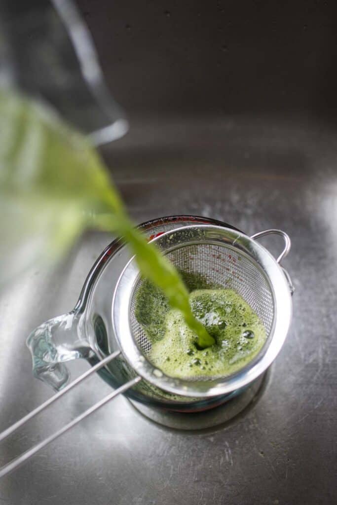 Green pandan water pouring through a sieve. 