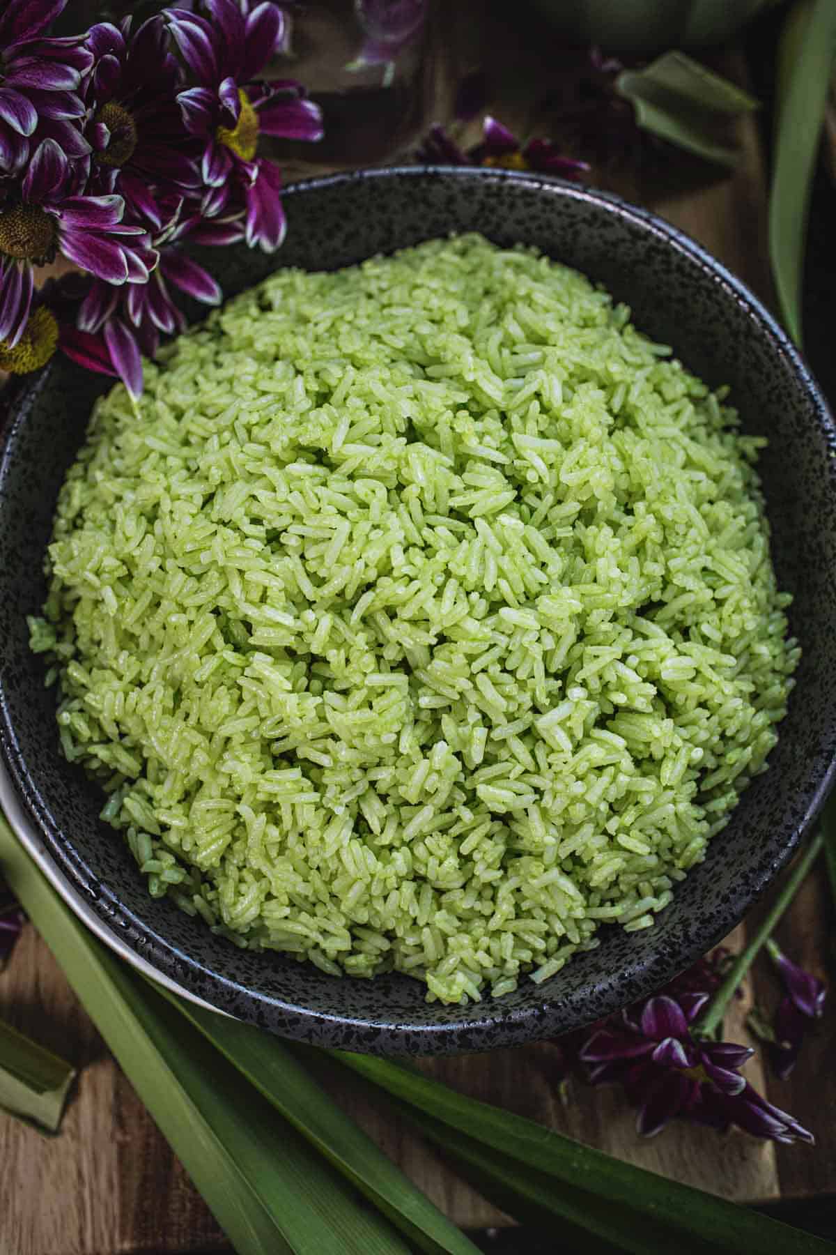 Pandan jasmine rice in a black bowl with flowers around.