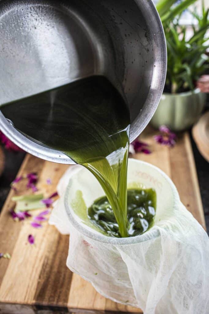 Pot pouring pandan water into cheesecloth. 