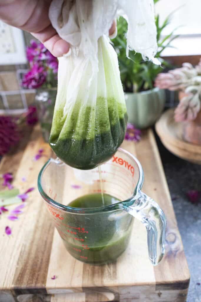 Cheesecloth straining green pandan juice into a pyrex cup.