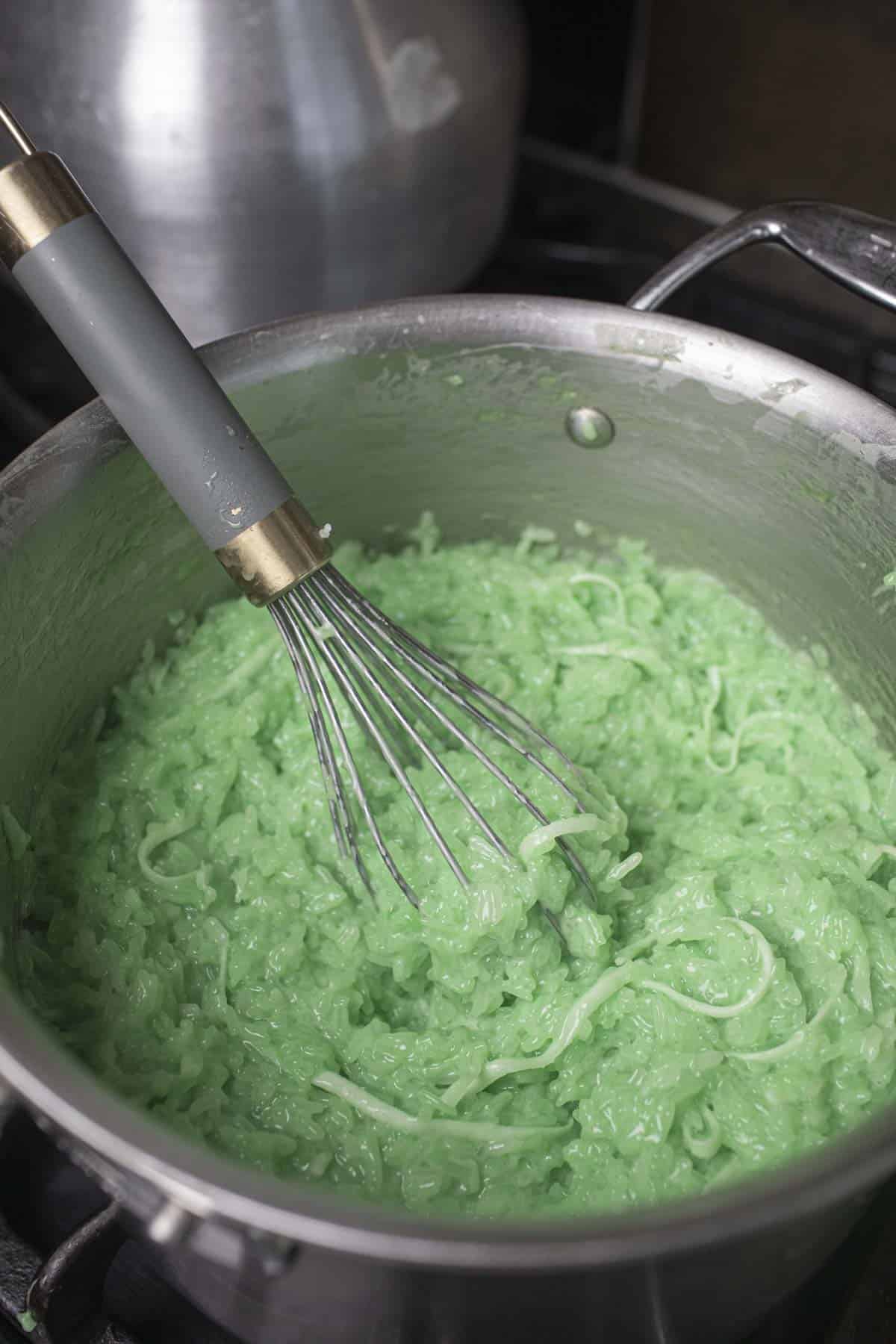 Green pandan sticky rice dessert in a pot with a whisk.