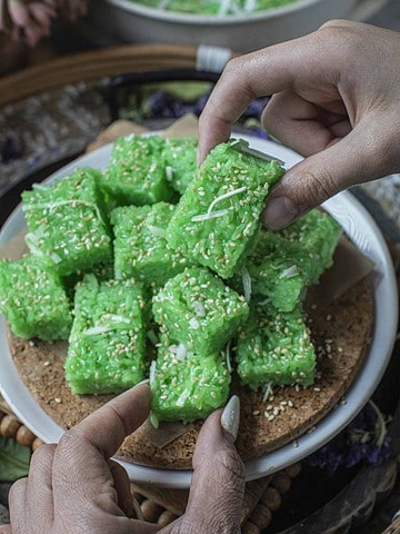 Hands lifting Thai pandan coconut sticky rice cubes.
