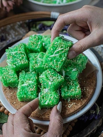 Hands lifting Thai pandan coconut sticky rice cubes.