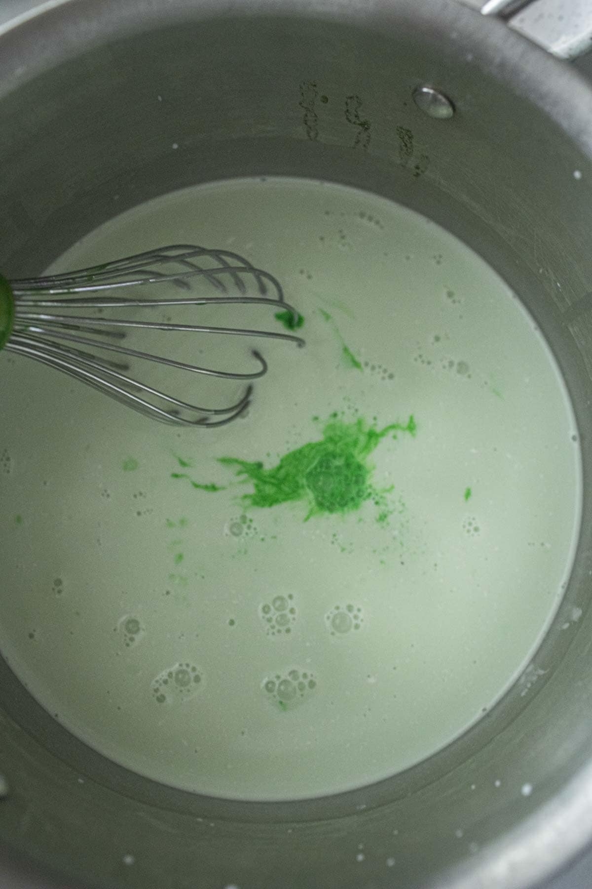 coconut milk and green pandan coloring in a sauce pan.