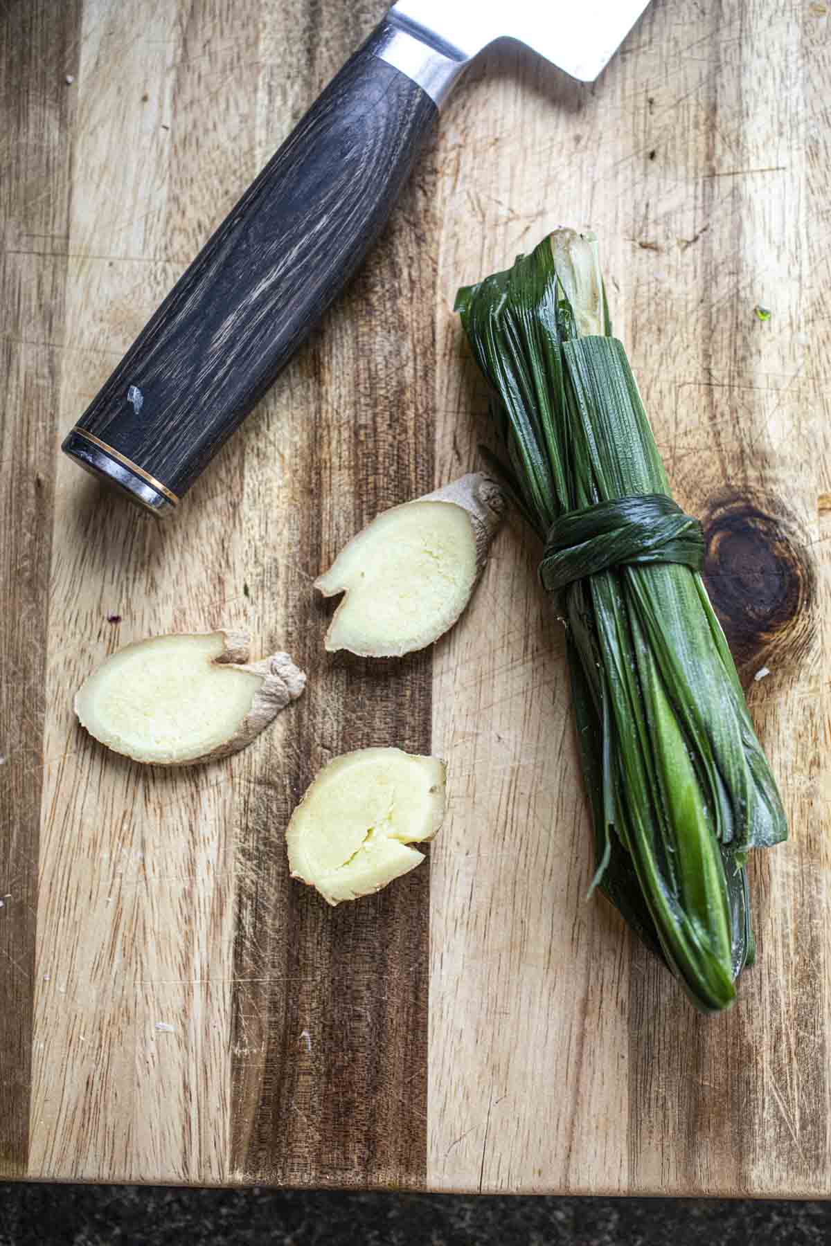 Ginger slices and pandan leaves on a cutting board. 