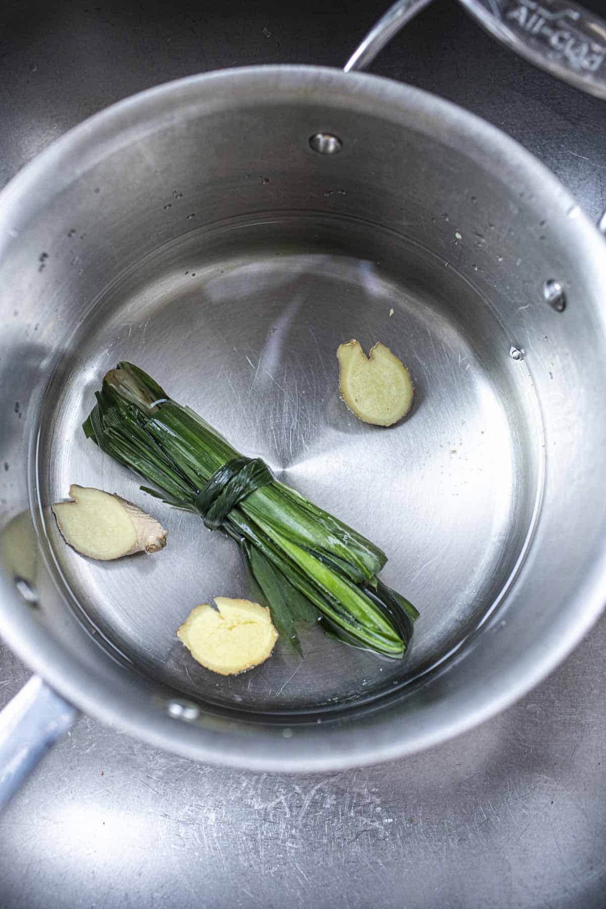 Water in a pot with pandan leaves and ginger slices.