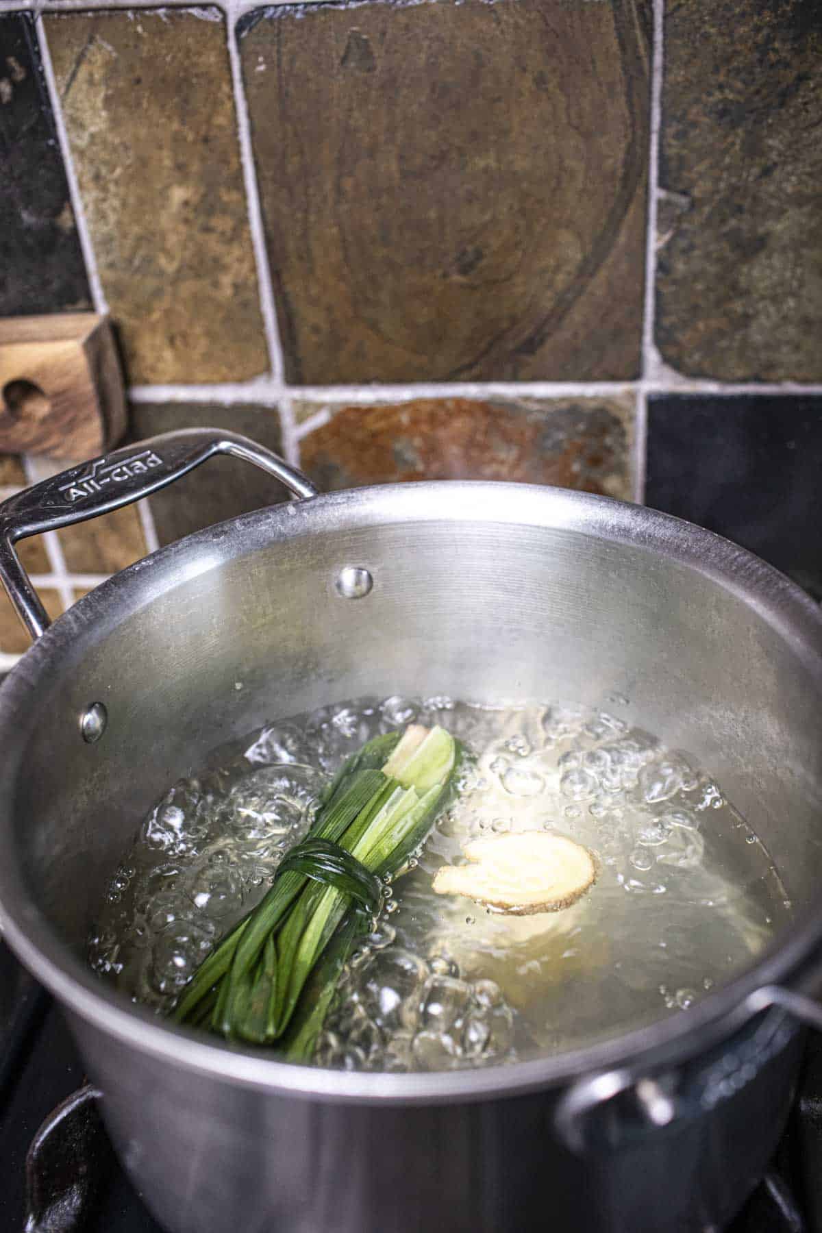 Boling water in a pot with pandan leaves and ginger slice.  