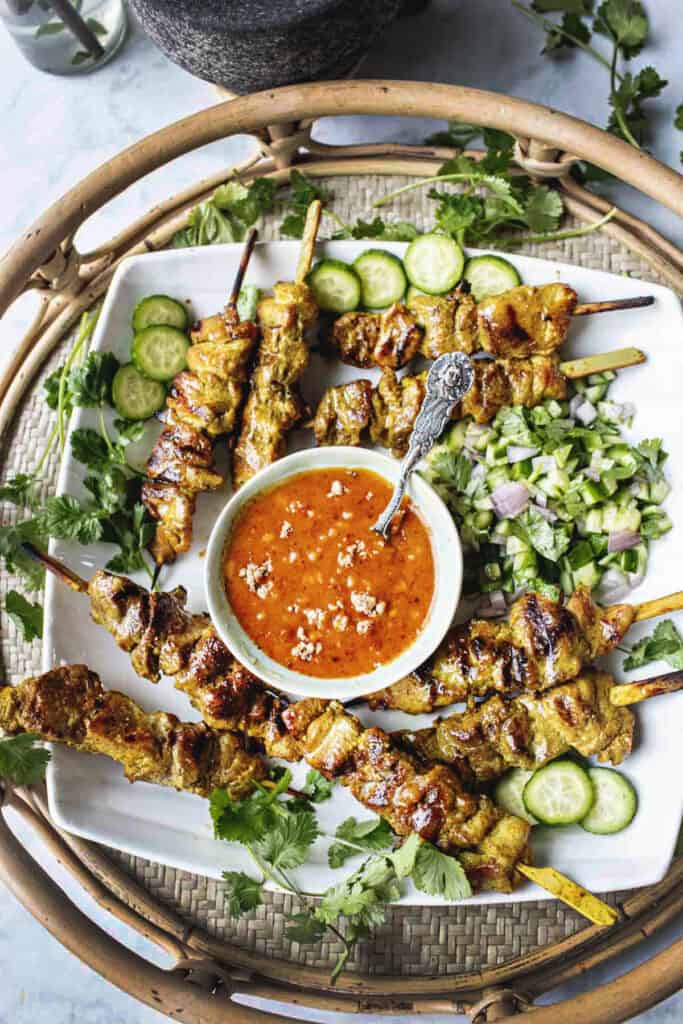 Thai pork satay skewers with dipping sauced on a tray.