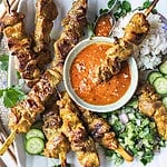 Pork satay on skewers on a platter with serving sauce.