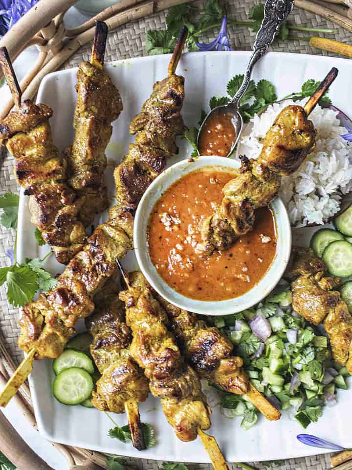Pork satay on skewers on a platter with serving sauce.