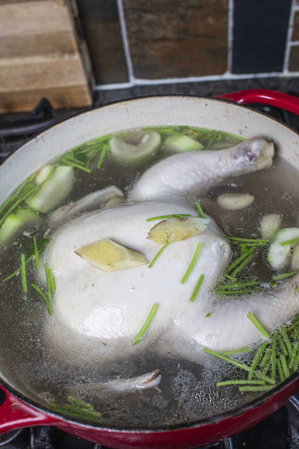 Whole chicken in broth in a pot with herbs. 