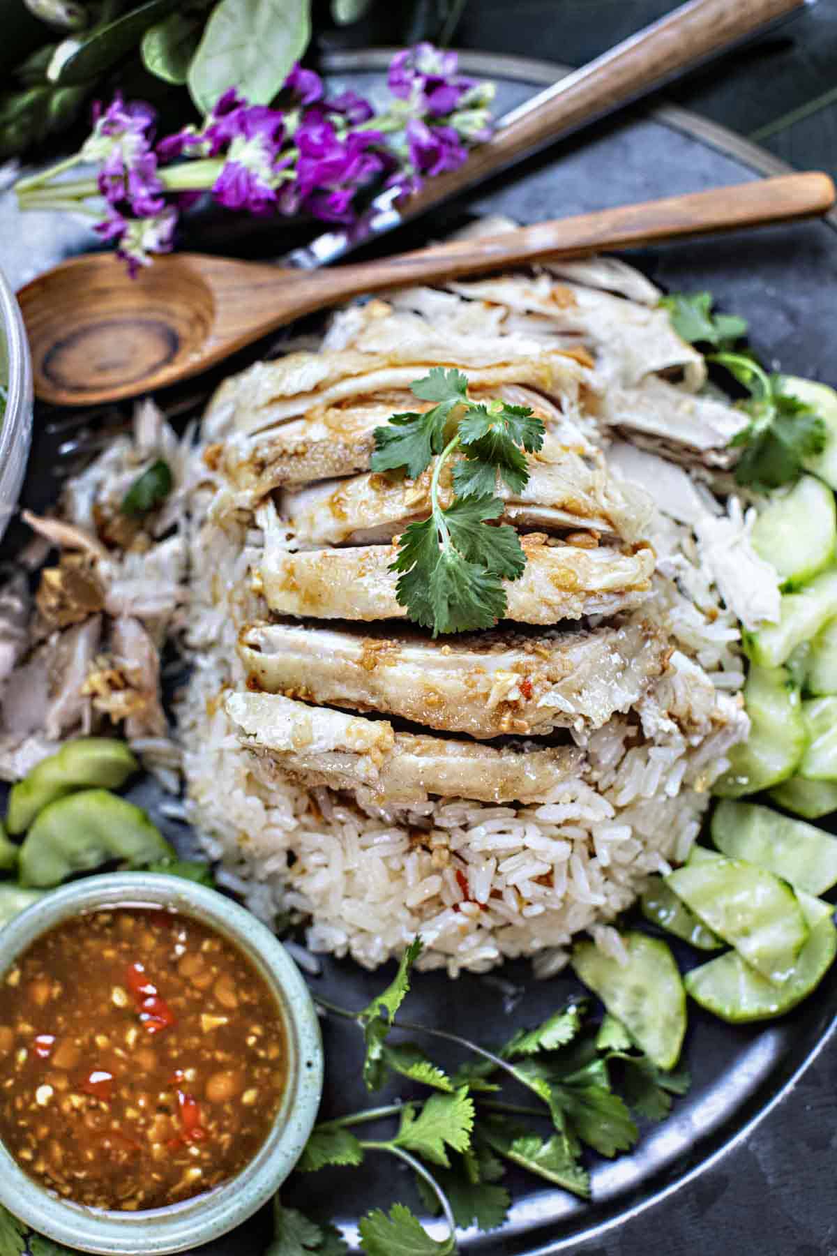 Thai chicken rice on a plate with cucumbers and sauce on the side. 