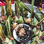 Leaf wrapped pandan chicken on platter with dipping sauce.