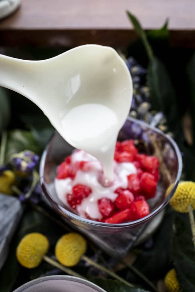 A spoon pouring coconut milk into a Thai red rubies dessert in a bowl. 