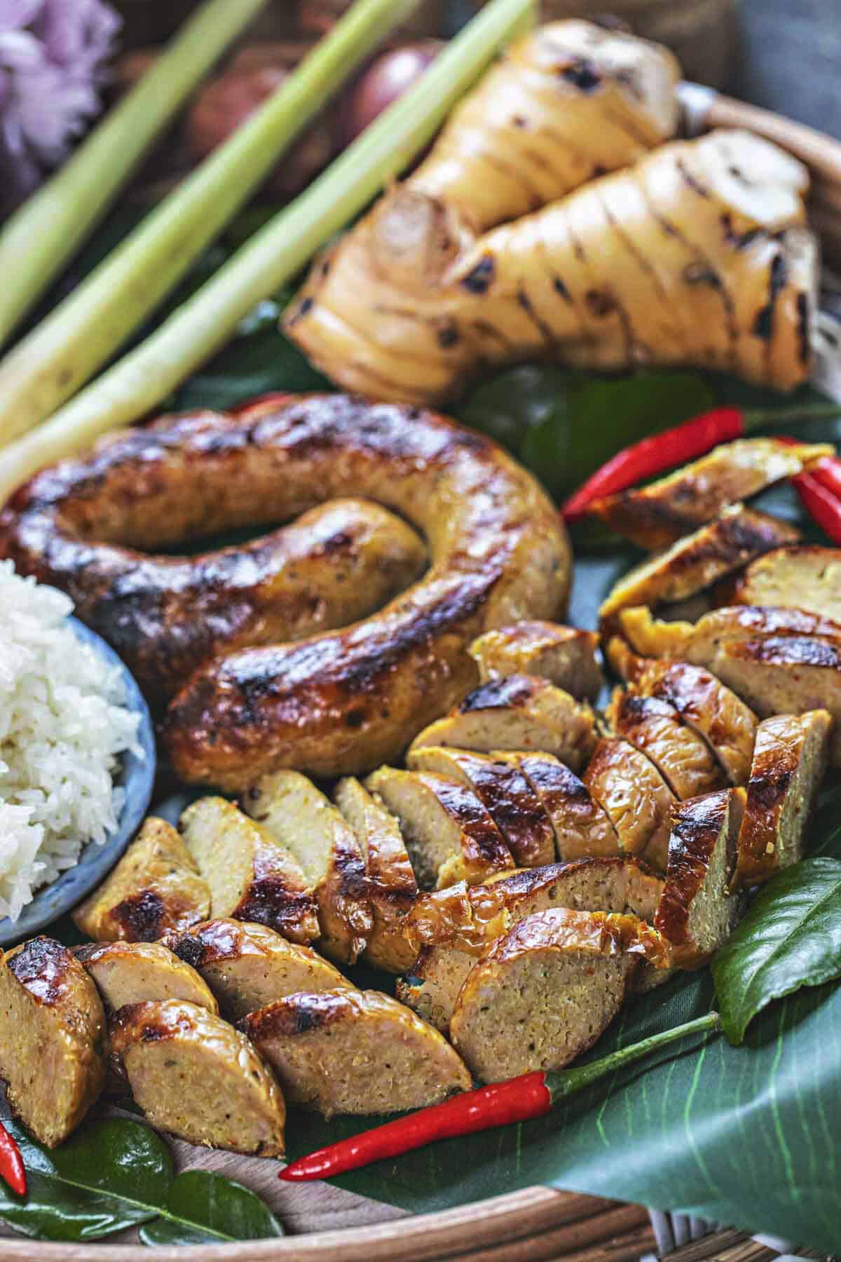 Sausage slices on a banana leaf with chilis, rice and leaves.