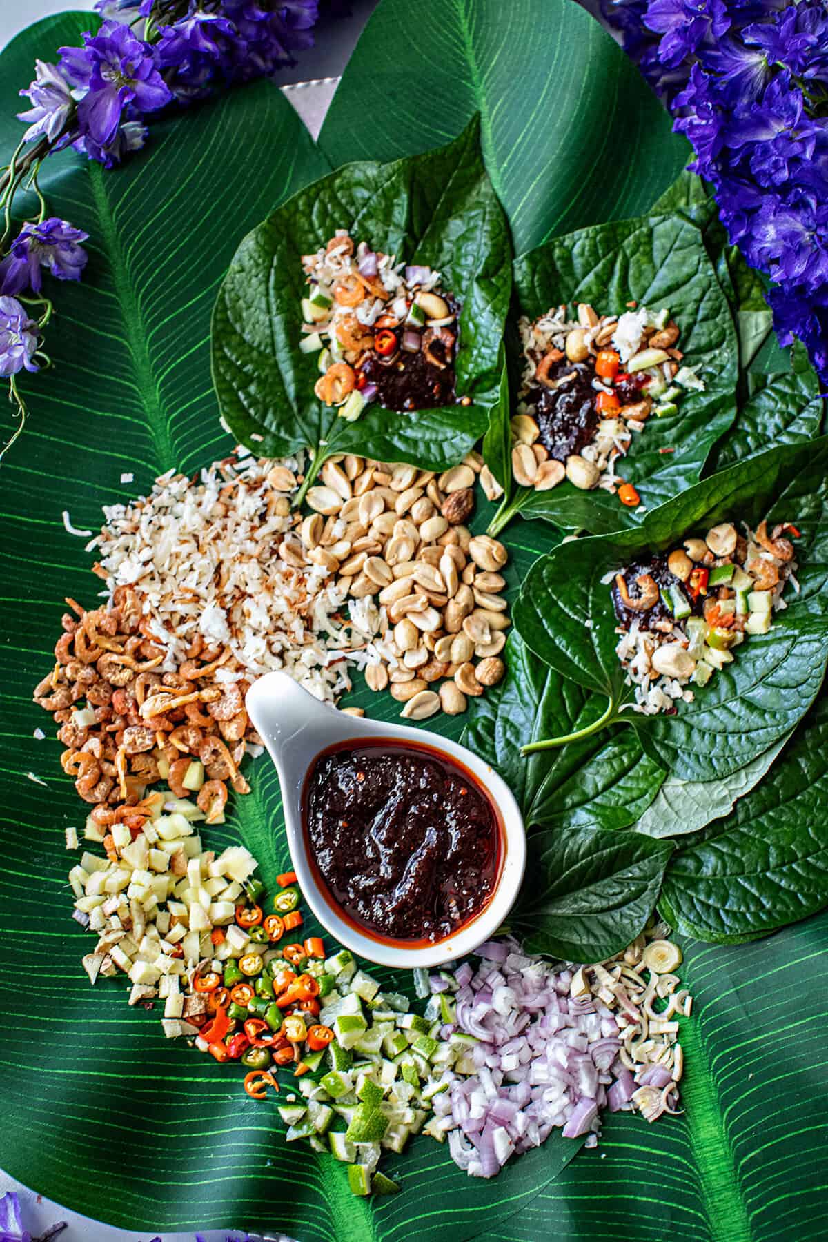 Miang Kham Thai betel leave wrap on a platter with ingredients around a dipping sauce.