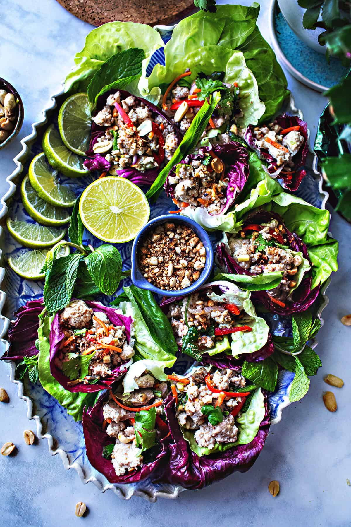 Thai pork lettuce wrap on a platter with lime wedges and peanuts. 