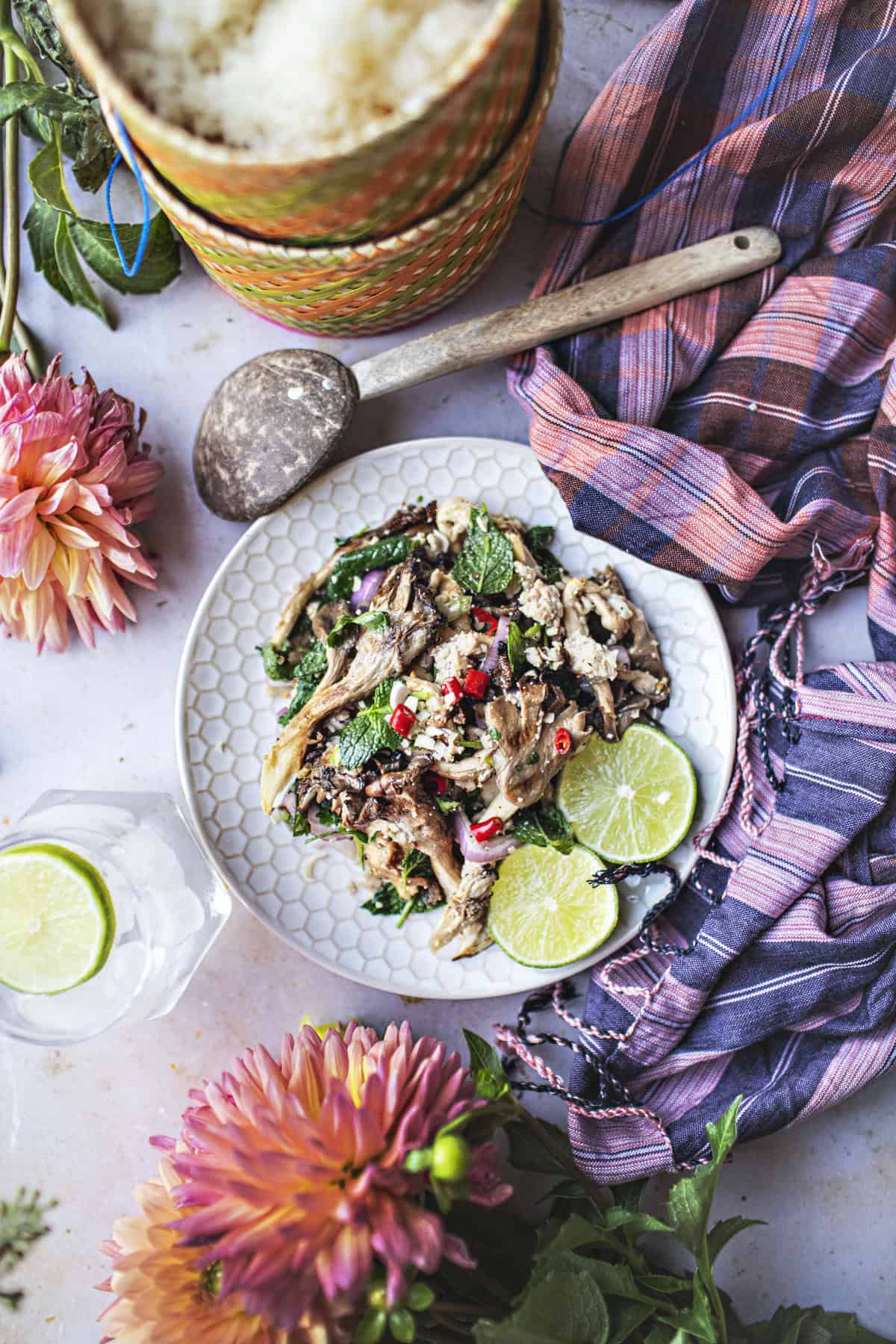 Oyster mushroom larb salad on a plate with lime wedges on the table. 