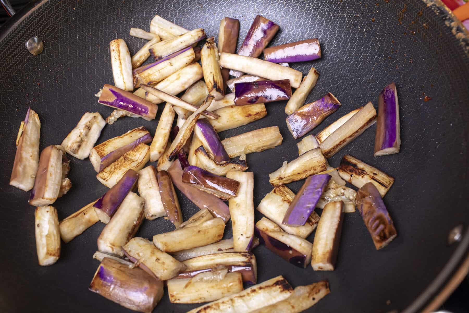 Cooked purple eggplant pieces in a wok.