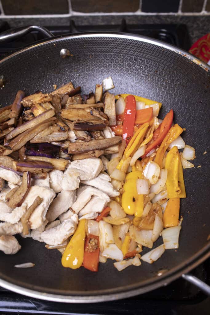 Cooked onion and bell pepper, chicken, and eggplant pieces in a wok.