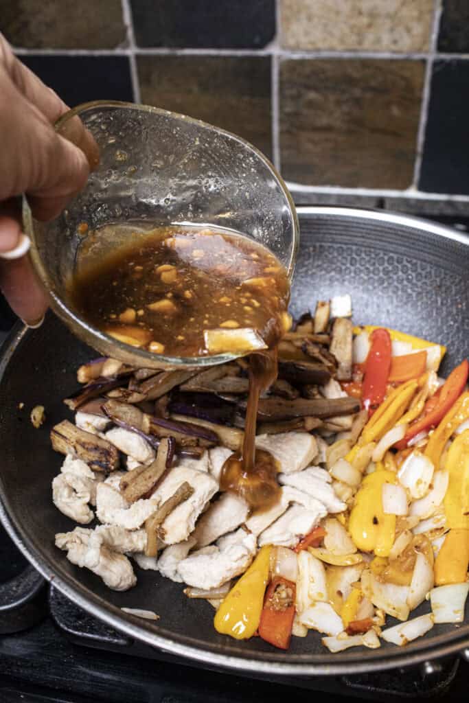 Sauce pouring into a wok with chicken and pepper. 