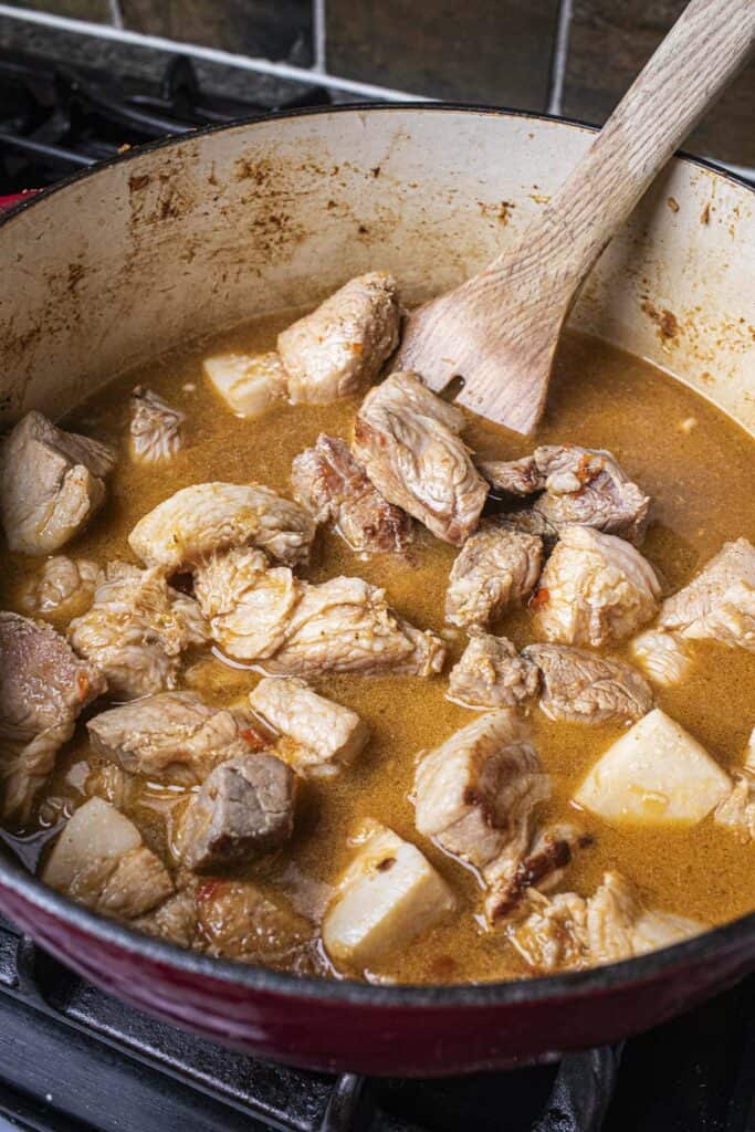 Spatula with pork chunks with hung lay curry in a dutch oven.