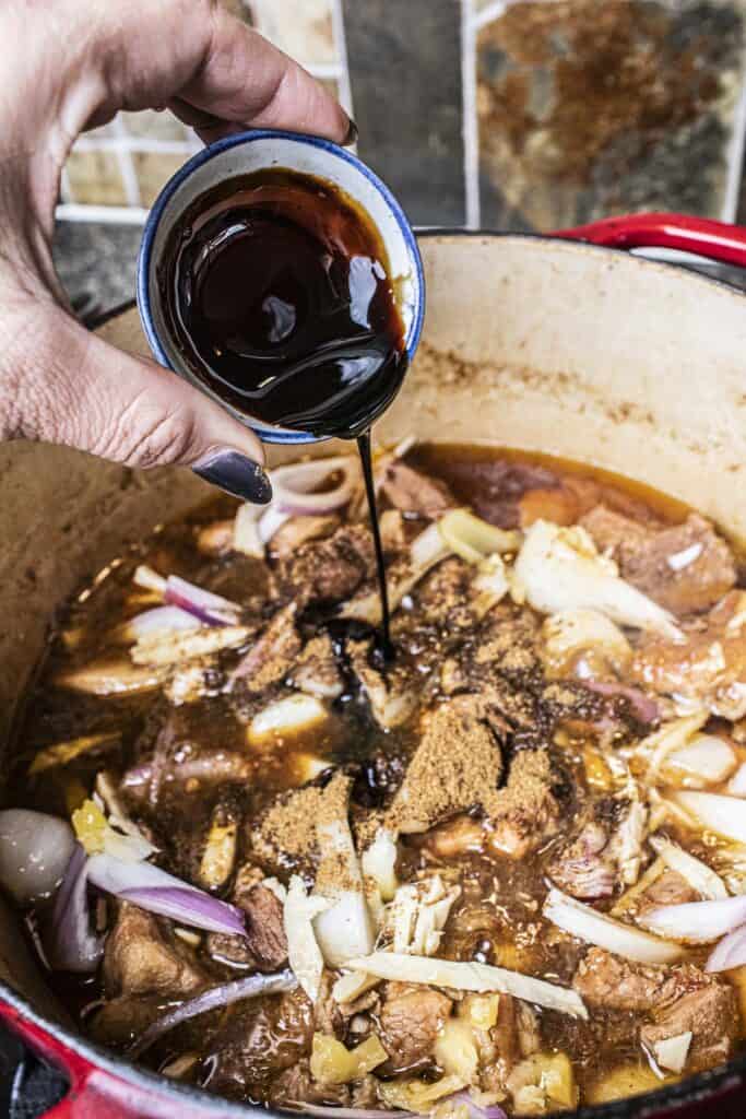 Sauce pouring into hung lay curry in a dutch oven.