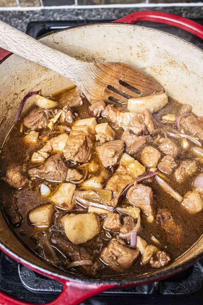 Spatula with pork chunks with hung lay curry in a dutch oven.