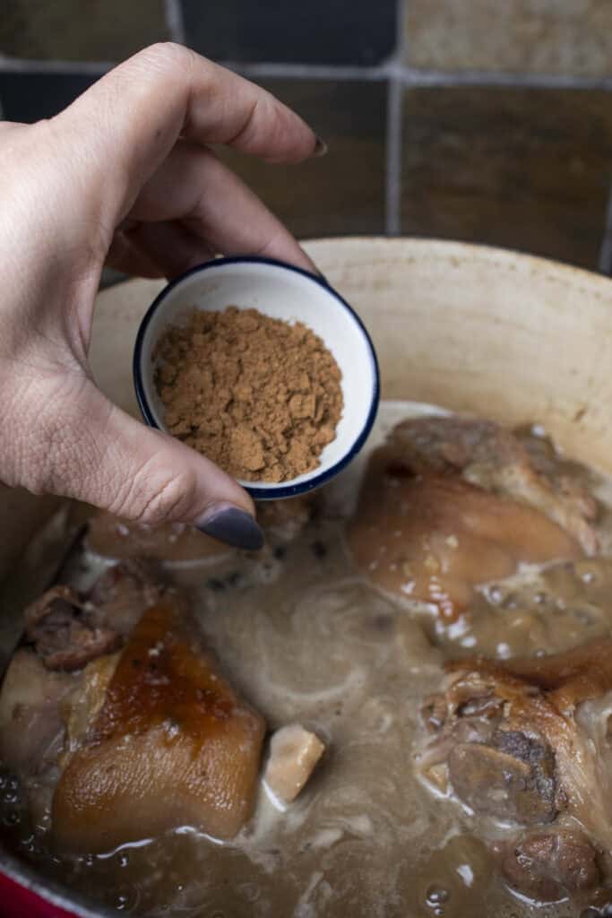 Five spice powder pouring into a pot with pork hocks.