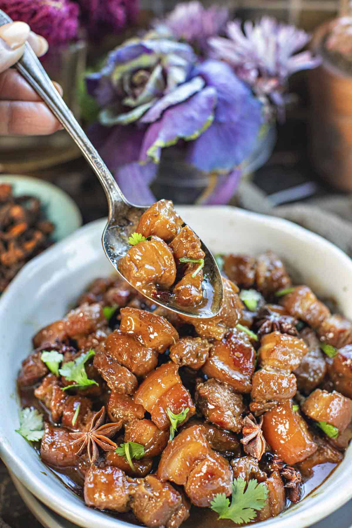A spoon lifting pork belly cubes from a bowl.