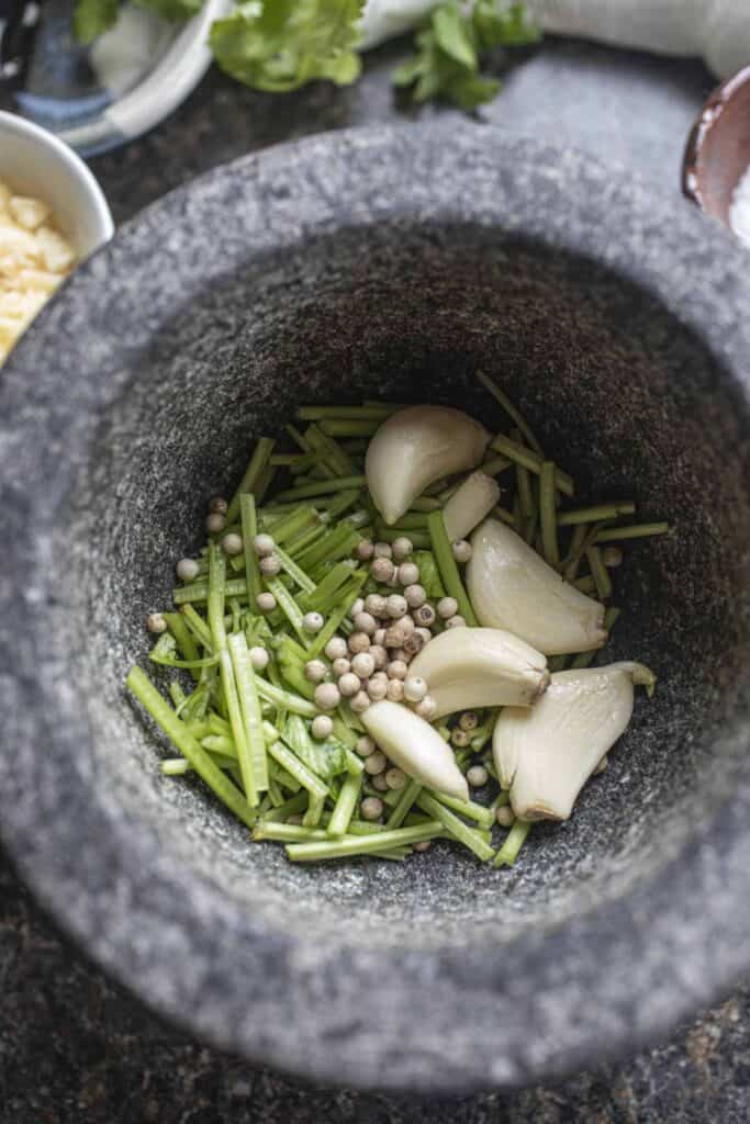 Garlic, cilantro stems and white peppercorn in a mortar.