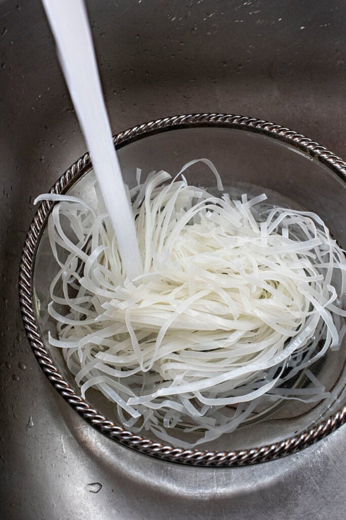 Rice noodles for Pad Thai in a bowl with running water. 