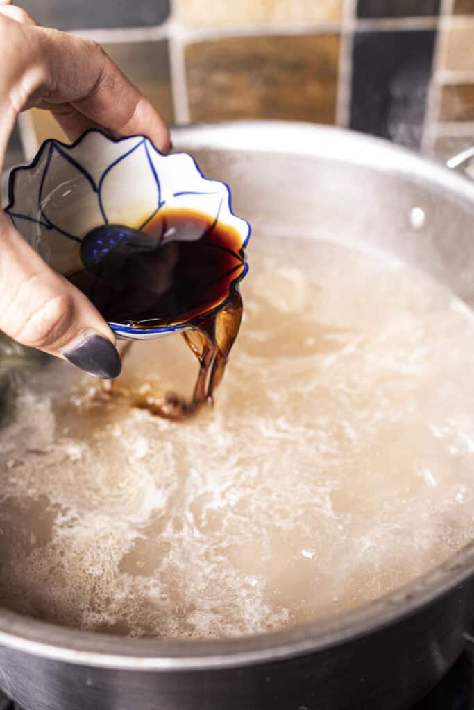 Soy sauce pouring into a broth  for Thai boat noodle soup in a pot.