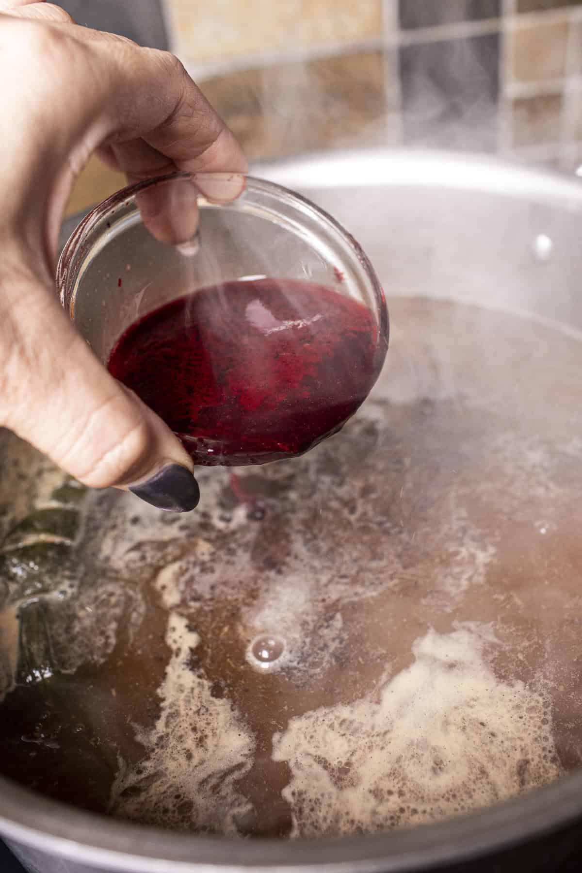 Blood in a cup pouring into a broth  for Thai boat noodle soup in a pot.