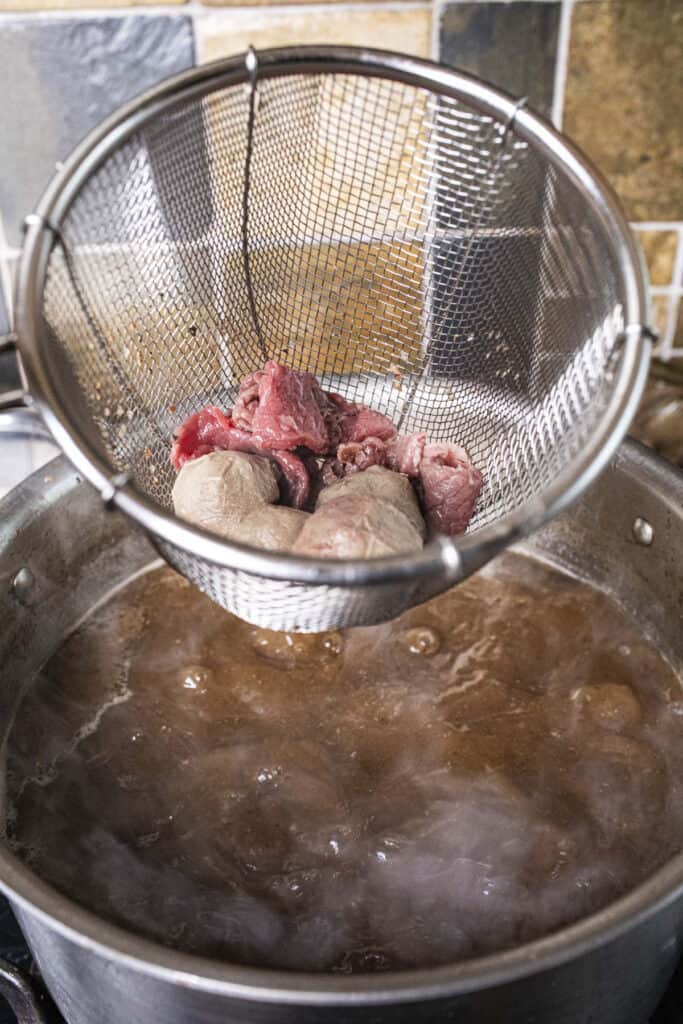 Meat balls and sliced meat in a wire basket over a broth in a pot.  