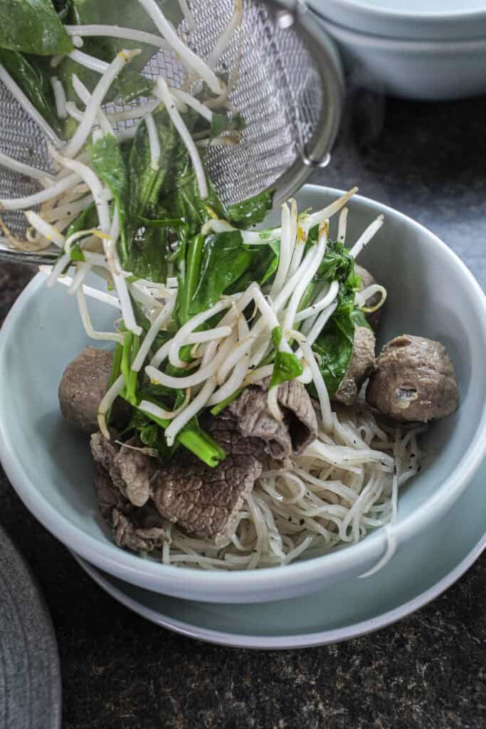 Blanched Bean sprouts and water spinach in a metal basket pouring into a bowl. 