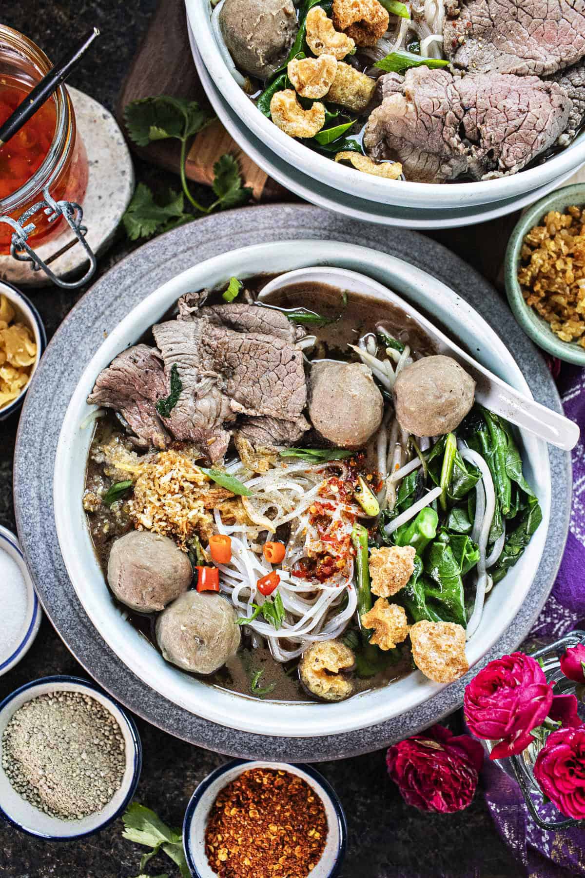 2 bowls of boat noodles soup wih meat, noodles and veggies in a bowl. 