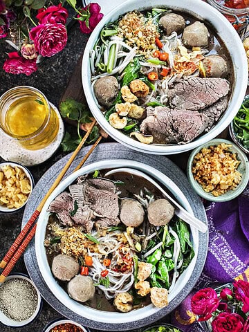 Boat Noodles in two bowls with garnishes on the sides.