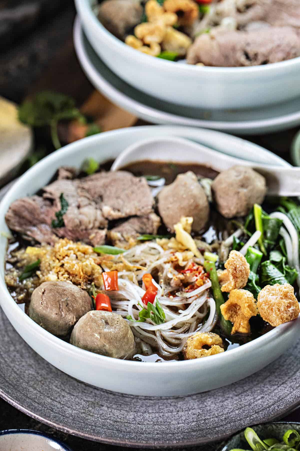 A bowl of boat noodles wih meat, noodles and veggies in a bowl. 