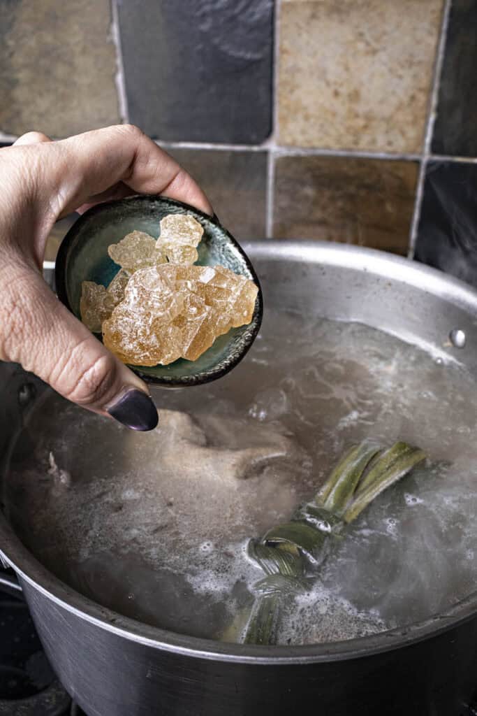 Rock sugar, pandan leaves and pork bones for Thai boat noodle soup in a pot.