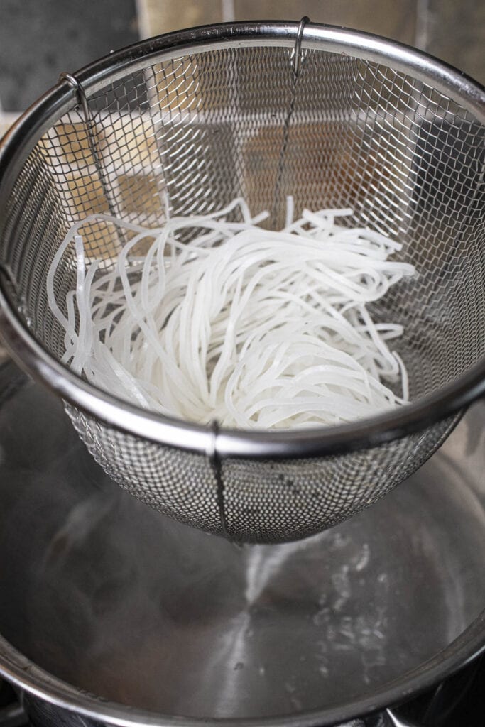 Rice noodles in a basket over hot wate in a pot.  