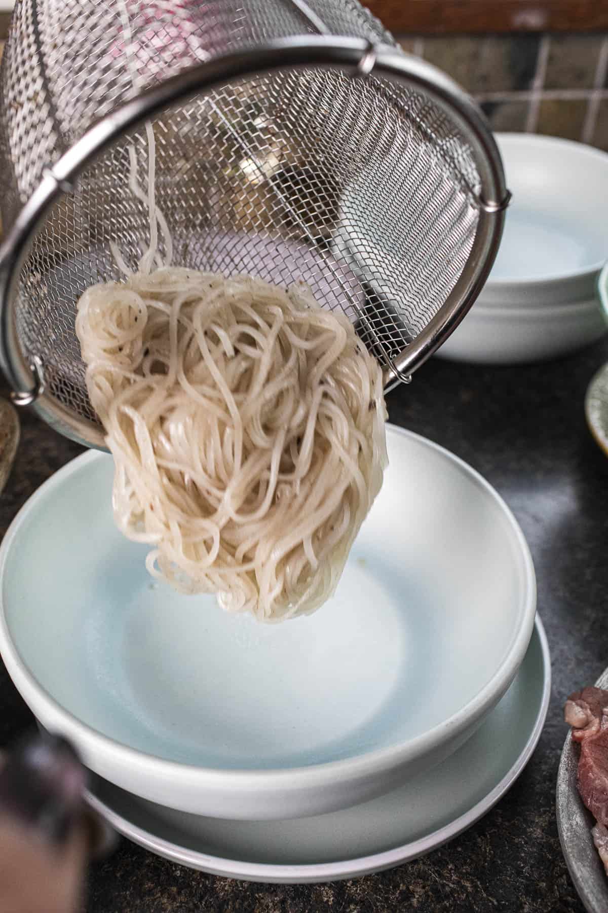 Rice noodles in a basket pouring into a bowl. 