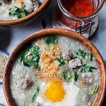 Jok Thai rice porridge in a bowl with eggs and herbs.